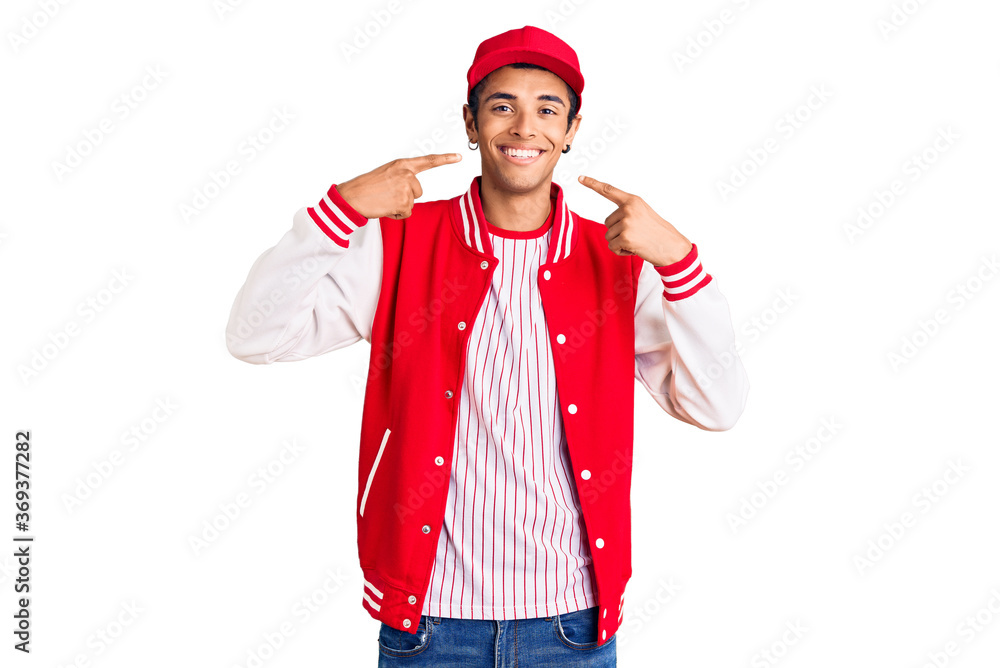 Young african amercian man wearing baseball uniform smiling cheerful showing and pointing with fingers teeth and mouth. dental health concept.