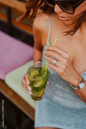 Beautiful attractive caucasian woman with sunglasses in a silver summer dress drinking a cocktail in a cafe