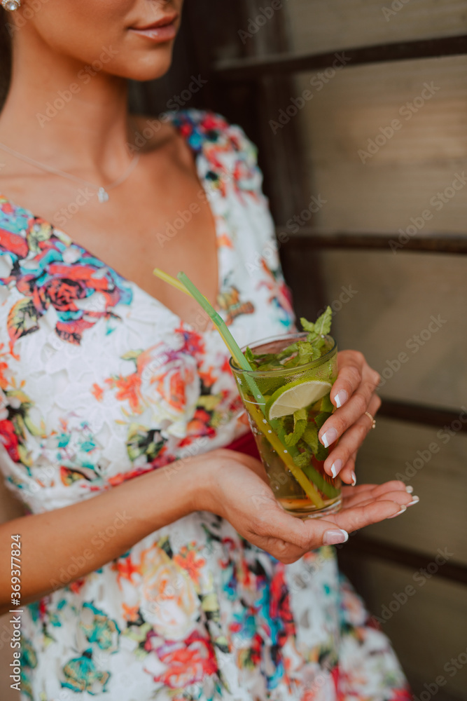 Obraz premium A beautiful sensual caucasian woman in a summer dress drinks a mojito cocktail in a cafe