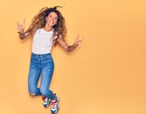 Young beautiful woman with tattoo wearing casual clothes smiling happy. Jumping with smile on face doing rocker sign over isolated yellow background