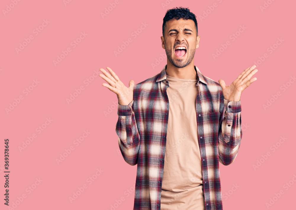 Young hispanic man wearing casual clothes celebrating mad and crazy for success with arms raised and closed eyes screaming excited. winner concept Young hispanic man wearing casual clothes celebrating mad and crazy for success with arms raised and closed eyes screaming excited. winner concept