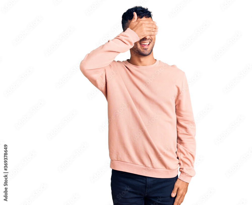 Young hispanic man wearing casual clothes smiling and laughing with hand on face covering eyes for surprise. blind concept. Young hispanic man wearing casual clothes smiling and laughing with hand on face covering eyes for surprise. blind concept.