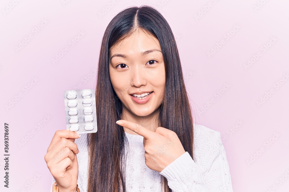 Young beautiful chinese woman holding pills smiling happy pointing with hand and finger Young beautiful chinese woman holding pills smiling happy pointing with hand and finger