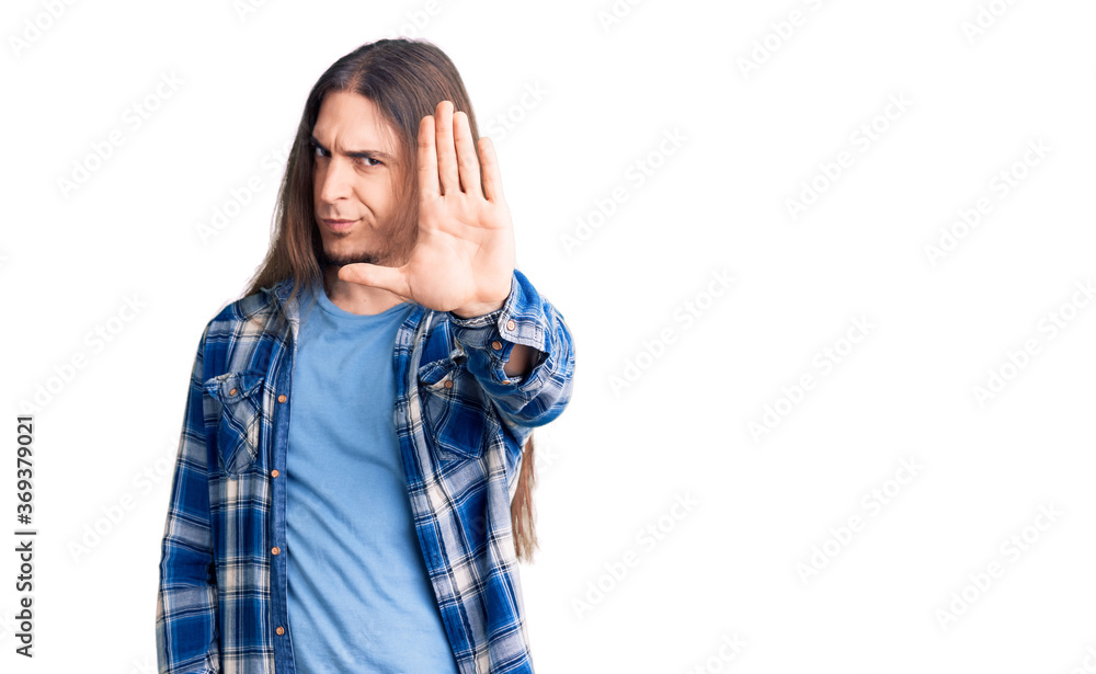 Young adult man with long hair wearing casual shirt doing stop sing with palm of the hand. warning expression with negative and serious gesture on the face. Young adult man with long hair wearing casual shirt doing stop sing with palm of the hand. warning expression with negative and serious gesture on the face.