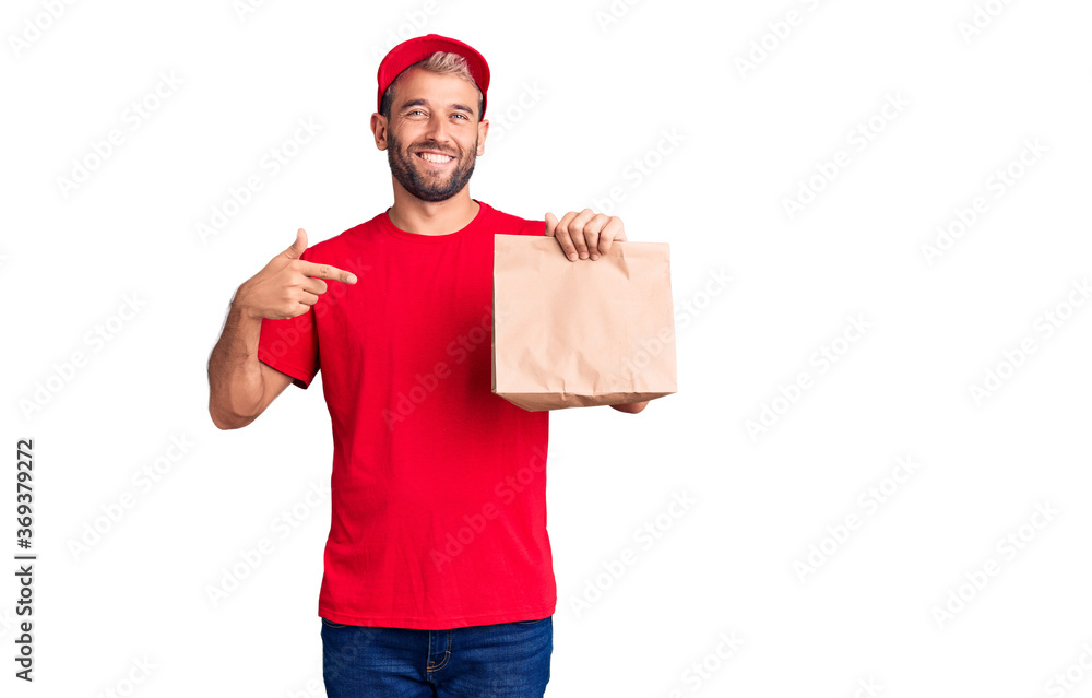 Young handsome blond man holding delivery paper bag pointing finger to one self smiling happy and proud