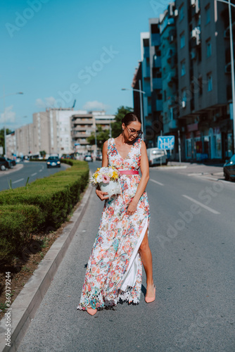 Young beautiful stylish caucasian woman model in summer dress with flower box in her hand on the street © Dragica