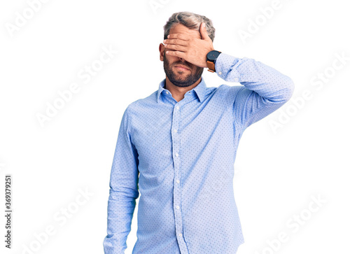 Young handsome blond man wearing elegant shirt covering eyes with hand, looking serious and sad. sightless, hiding and rejection concept