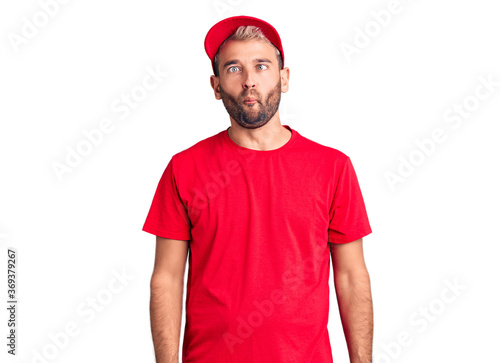 Young handsome blond man wearing t-shirt and cap making fish face with lips, crazy and comical gesture. funny expression.