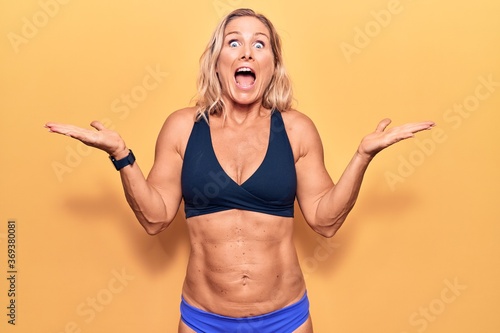 Middle age caucasian blonde woman wearing bikini celebrating victory with happy smile and winner expression with raised hands