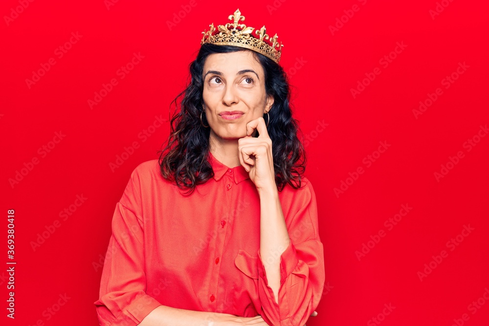 Young beautiful hispanic woman wearing princess crown thinking concentrated about doubt with finger on chin and looking up wondering Young beautiful hispanic woman wearing princess crown thinking concentrated about doubt with finger on chin and looking up wondering