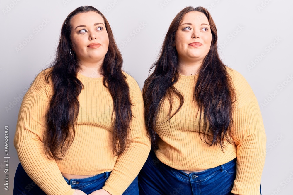 Young plus size twins wearing casual clothes smiling looking to the side and staring away thinking. Young plus size twins wearing casual clothes smiling looking to the side and staring away thinking.