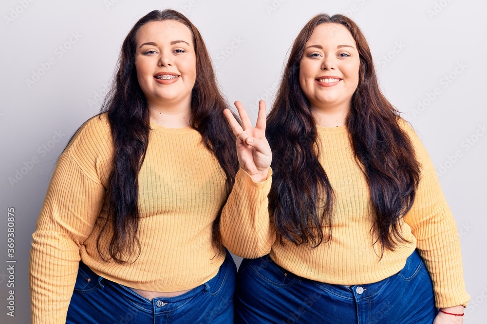 Young plus size twins wearing casual clothes showing and pointing up with fingers number three while smiling confident and happy. Young plus size twins wearing casual clothes showing and pointing up with fingers number three while smiling confident and happy.