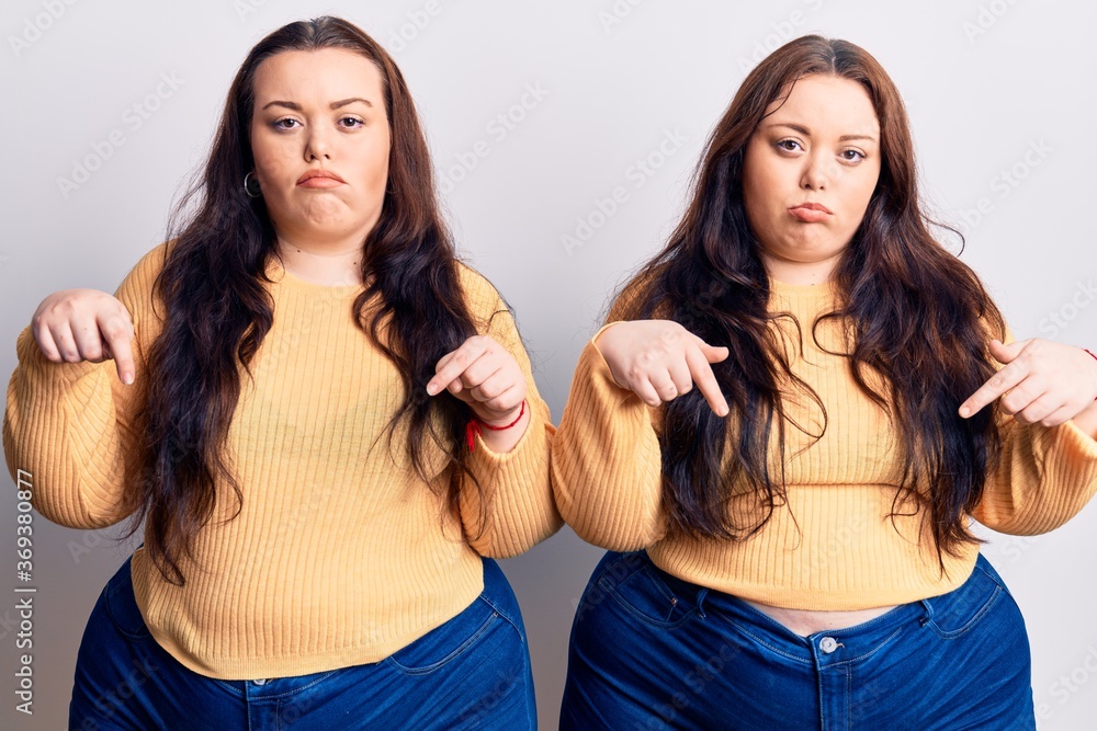 Young plus size twins wearing casual clothes pointing down looking sad and upset, indicating direction with fingers, unhappy and depressed. Young plus size twins wearing casual clothes pointing down looking sad and upset, indicating direction with fingers, unhappy and depressed.