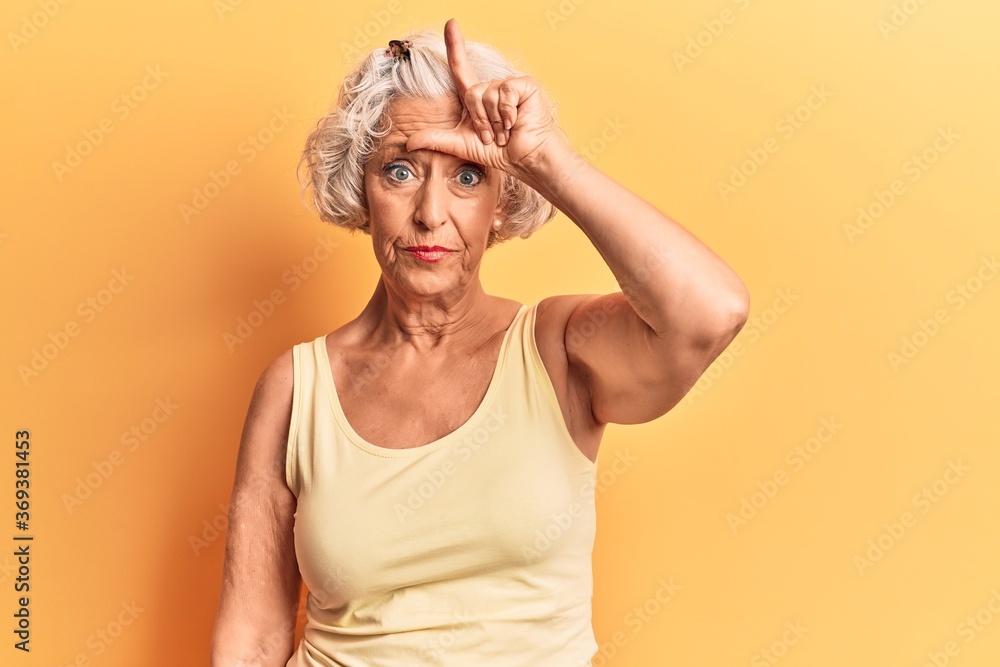 Senior grey-haired woman wearing casual clothes making fun of people with fingers on forehead doing loser gesture mocking and insulting. Senior grey-haired woman wearing casual clothes making fun of people with fingers on forehead doing loser gesture mocking and insulting.