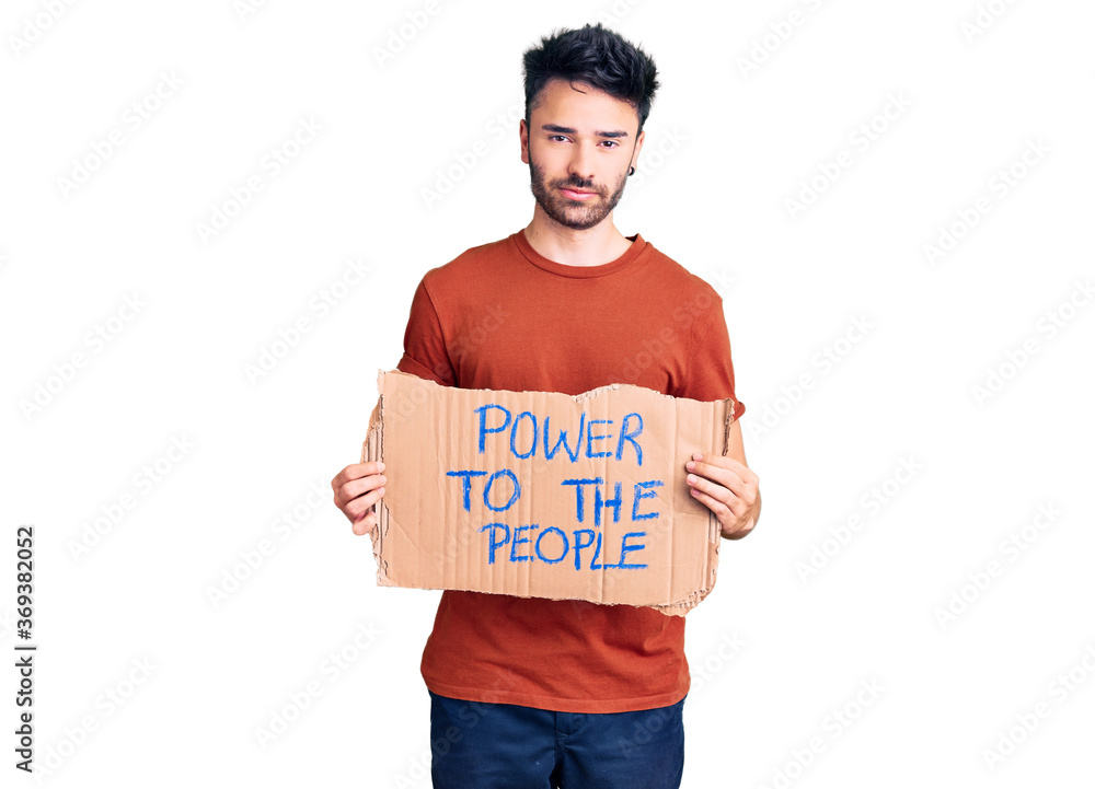 Young hispanic man holding power to the people banner thinking attitude and sober expression looking self confident Young hispanic man holding power to the people banner thinking attitude and sober expression looking self confident