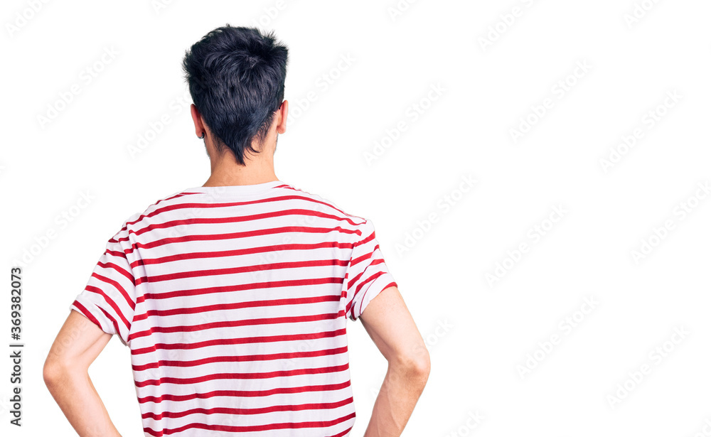 Young hispanic man wearing casual clothes standing backwards looking away with arms on body Young hispanic man wearing casual clothes standing backwards looking away with arms on body
