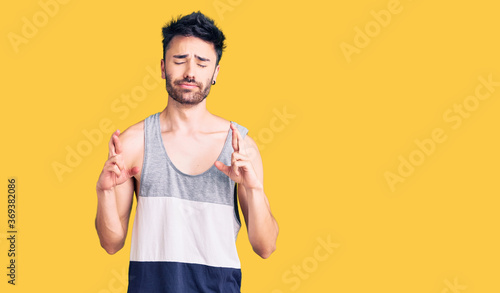 Young hispanic man wearing casual clothes gesturing finger crossed smiling with hope and eyes closed. luck and superstitious concept.