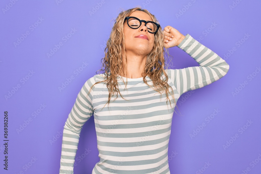 Beautiful blonde woman wearing casual striped t-shirt and glasses over purple background stretching back, tired and relaxed, sleepy and yawning for early morning Beautiful blonde woman wearing casual striped t-shirt and glasses over purple background stretching back, tired and relaxed, sleepy and yawning for early morning