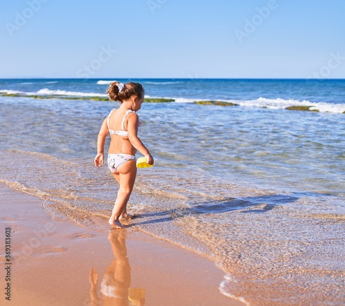 Adorable blonde child wearing bikini playing with water at the beach