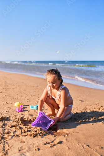 Adorable blonde child wearing bikini. Building sand castle using bucket and shovel at the beach © Krakenimages.com
