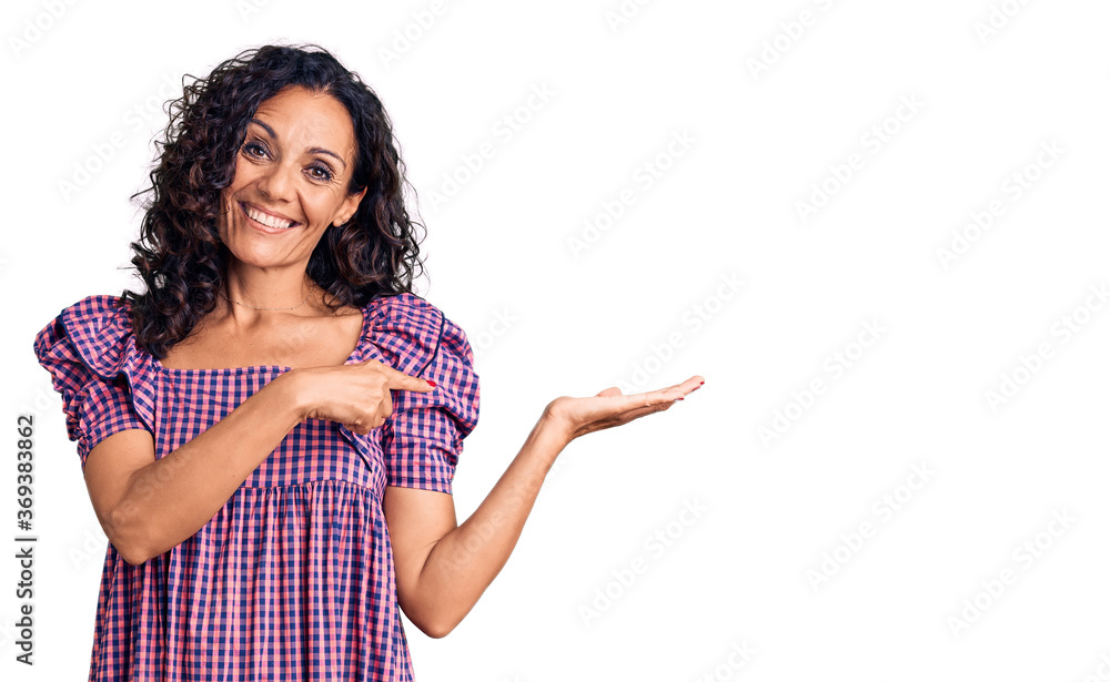 Middle age beautiful woman wearing casual dress amazed and smiling to the camera while presenting with hand and pointing with finger. Middle age beautiful woman wearing casual dress amazed and smiling to the camera while presenting with hand and pointing with finger.