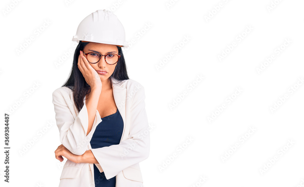 Young beautiful latin girl wearing architect hardhat and glasses thinking looking tired and bored with depression problems with crossed arms. Young beautiful latin girl wearing architect hardhat and glasses thinking looking tired and bored with depression problems with crossed arms.