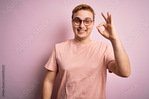 Young handsome redhead man wearing casual t-shirt standing over isolated pink background smiling positive doing ok sign with hand and fingers. Successful expression. © Krakenimages.com