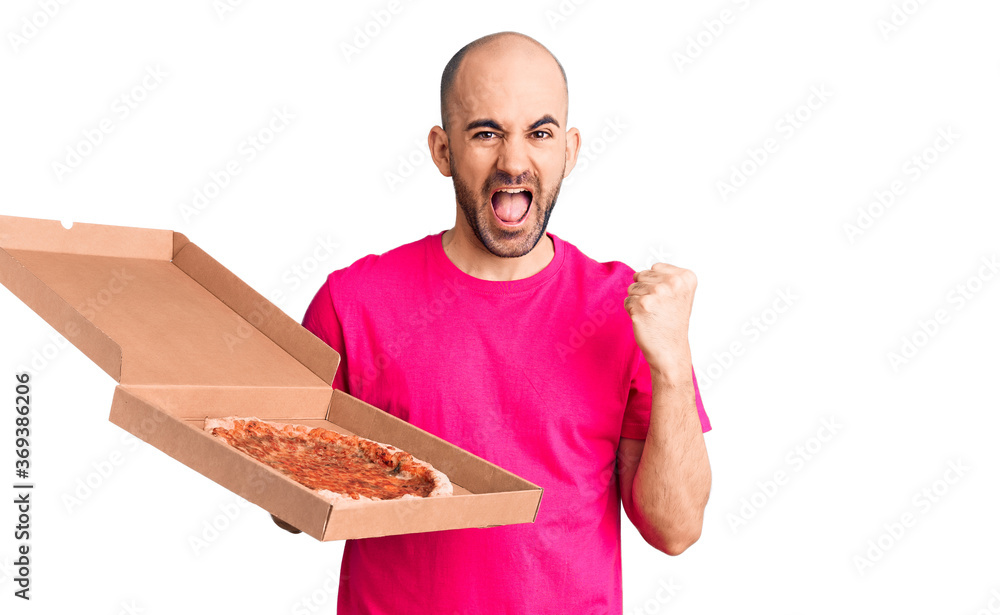 Young handsome man holding delivery pizza cardboard box screaming proud, celebrating victory and success very excited with raised arms Young handsome man holding delivery pizza cardboard box screaming proud, celebrating victory and success very excited with raised arms