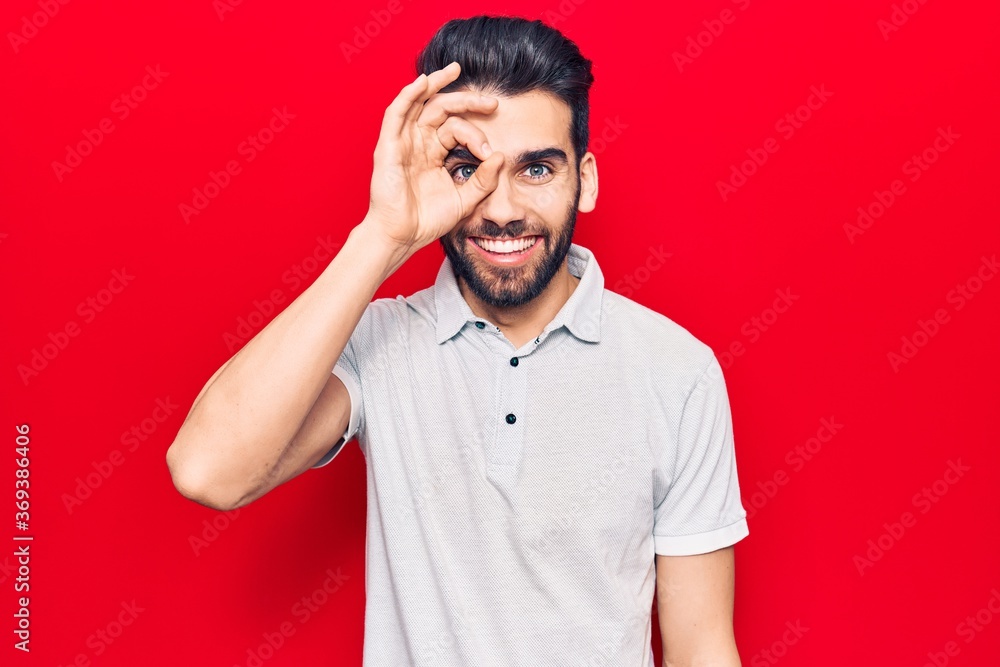 Young handsome man with beard wearing casual polo doing ok gesture with hand smiling, eye looking through fingers with happy face. Young handsome man with beard wearing casual polo doing ok gesture with hand smiling, eye looking through fingers with happy face.
