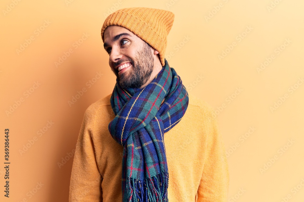Young handsome man with beard wearing wool cap and scarf looking away to side with smile on face, natural expression. laughing confident. Young handsome man with beard wearing wool cap and scarf looking away to side with smile on face, natural expression. laughing confident.