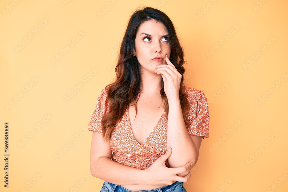 Young beautiful brunette woman wearing casual summer clothes serious face thinking about question with hand on chin, thoughtful about confusing idea Young beautiful brunette woman wearing casual summer clothes serious face thinking about question with hand on chin, thoughtful about confusing idea