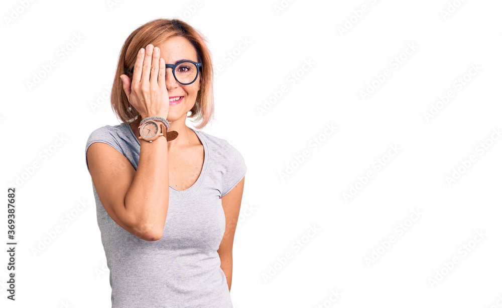 Young blonde woman wearing casual clothes covering one eye with hand, confident smile on face and surprise emotion. Young blonde woman wearing casual clothes covering one eye with hand, confident smile on face and surprise emotion.