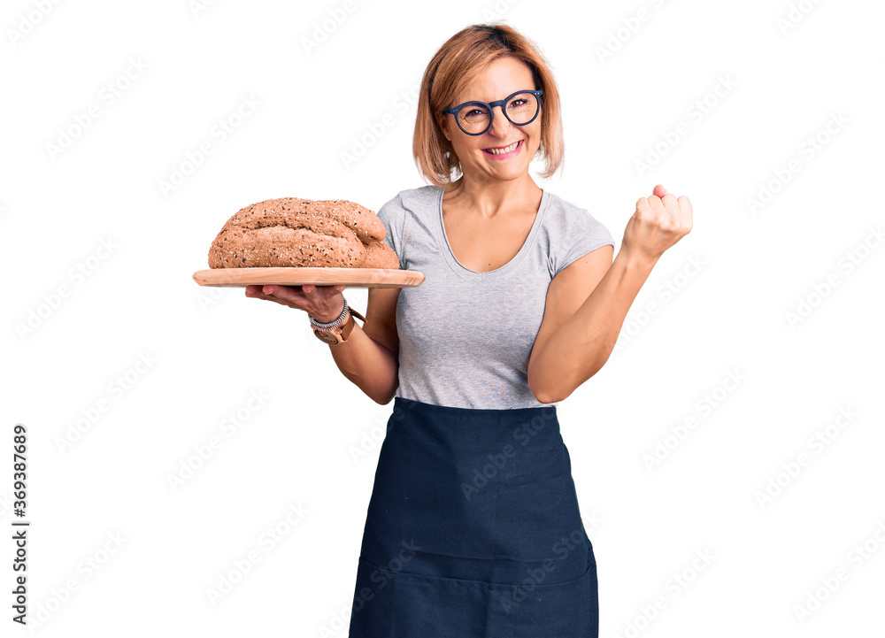 Young blonde woman holding wholemeal bread screaming proud, celebrating victory and success very excited with raised arms Young blonde woman holding wholemeal bread screaming proud, celebrating victory and success very excited with raised arms
