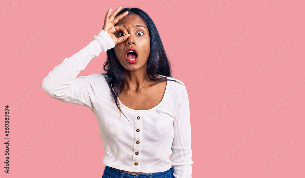 Young indian girl wearing casual clothes doing ok gesture shocked with surprised face, eye looking through fingers. unbelieving expression. Young indian girl wearing casual clothes doing ok gesture shocked with surprised face, eye looking through fingers. unbelieving expression.