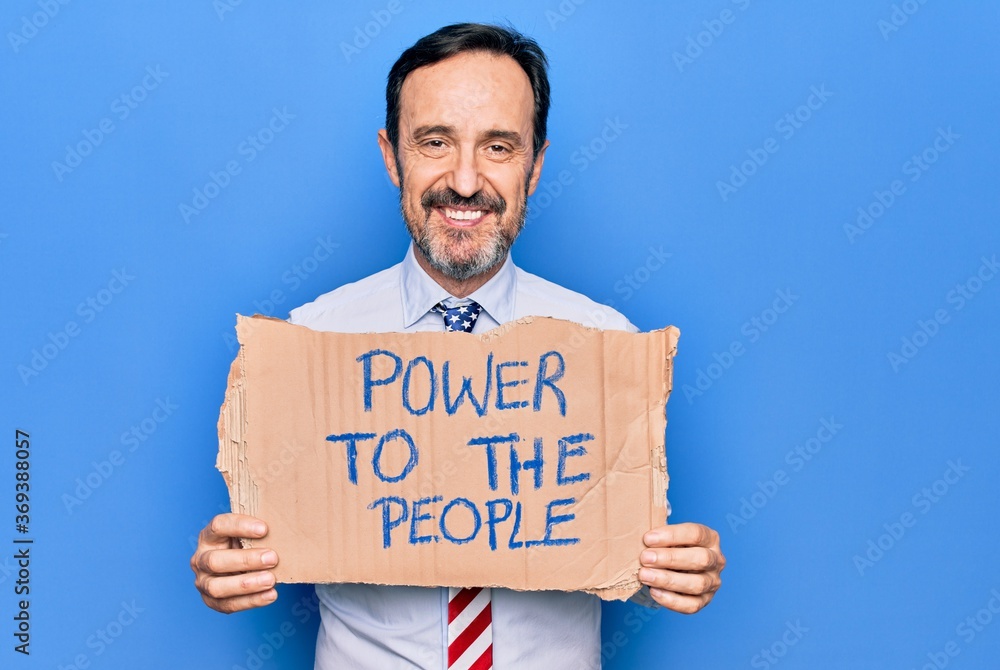 Middle age business man wearing usa tie holding banner with power to the people message looking positive and happy standing and smiling with a confident smile showing teeth Middle age business man wearing usa tie holding banner with power to the people message looking positive and happy standing and smiling with a confident smile showing teeth