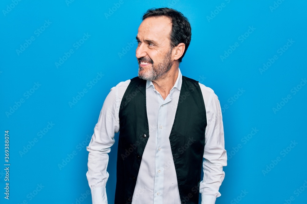 Middle age handsome man wearing elegant shirt and vest over isolated blue background looking to side, relax profile pose with natural face and confident smile. Middle age handsome man wearing elegant shirt and vest over isolated blue background looking to side, relax profile pose with natural face and confident smile.