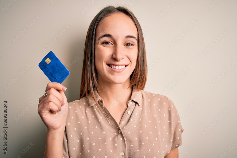 Young beautiful customer woman holding credit card to do payment over white background with a happy face standing and smiling with a confident smile showing teeth Young beautiful customer woman holding credit card to do payment over white background with a happy face standing and smiling with a confident smile showing teeth