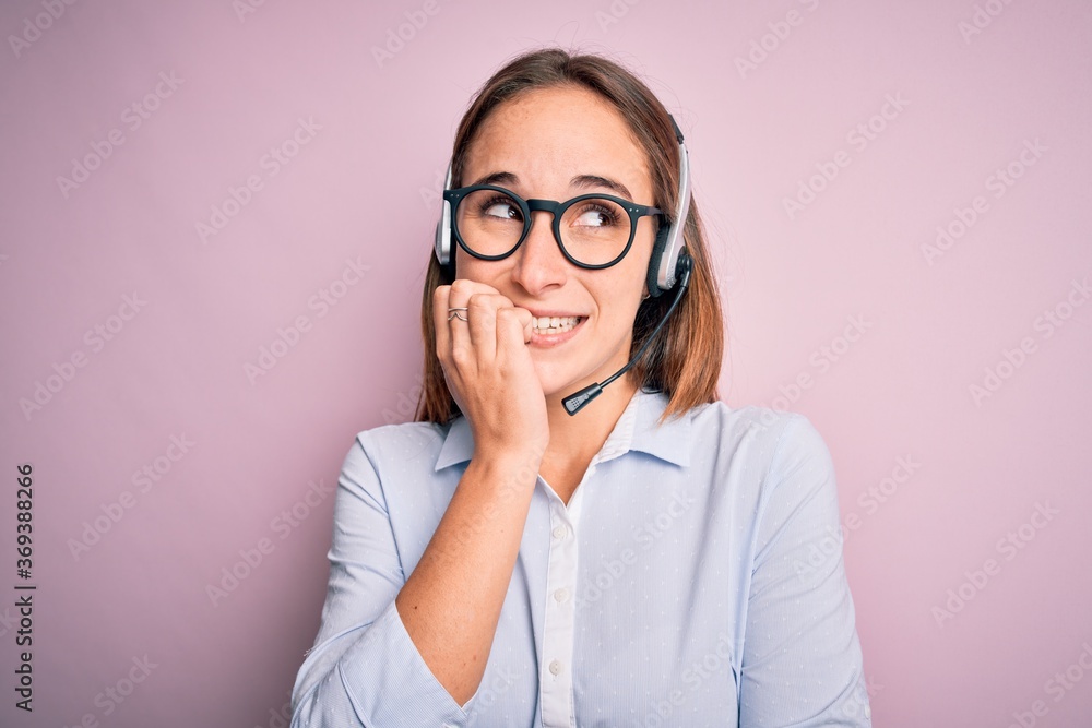 Young beautiful call center agent woman wearing glasses working using headset looking stressed and nervous with hands on mouth biting nails. Anxiety problem. Young beautiful call center agent woman wearing glasses working using headset looking stressed and nervous with hands on mouth biting nails. Anxiety problem.