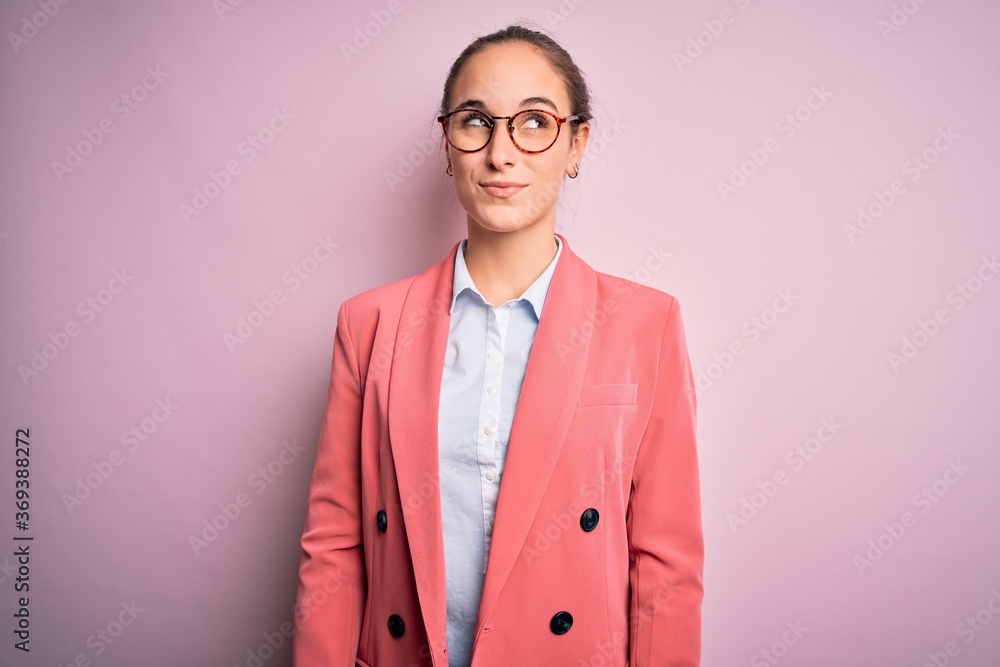 Young beautiful businesswoman wearing jacket and glasses over isolated pink background smiling looking to the side and staring away thinking. Young beautiful businesswoman wearing jacket and glasses over isolated pink background smiling looking to the side and staring away thinking.