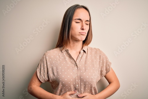 Young beautiful woman wearing casual shirt standing over isolated white background with hand on stomach because indigestion, painful illness feeling unwell. Ache concept.