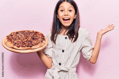 Beautiful child girl holding italian pizza celebrating victory with happy smile and winner expression with raised hands