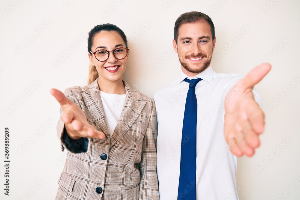 Beautiful couple wearing business clothes smiling cheerful offering palm hand giving assistance and acceptance. Beautiful couple wearing business clothes smiling cheerful offering palm hand giving assistance and acceptance.