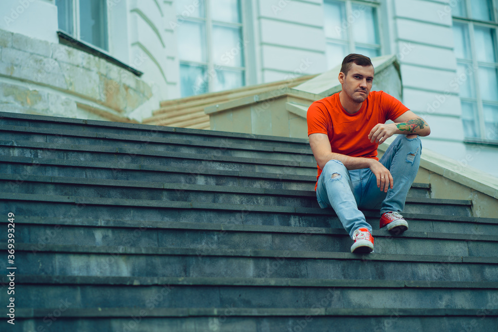 Adult man sitting on steps. Full body adult male in casual clothes looking at camera while sitting on stairs outside mansion Adult man sitting on steps. Full body adult male in casual clothes looking at camera while sitting on stairs outside mansion