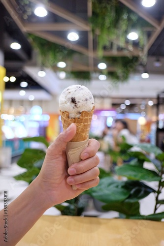 In selective focus a male hand holding a soft cone of ice cream with blurred the mall area and dark background 