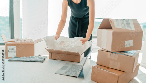 Selling clothing from home. Small business entrepreneur woman packing dress clothes in mailing box for shipping from online store. photo