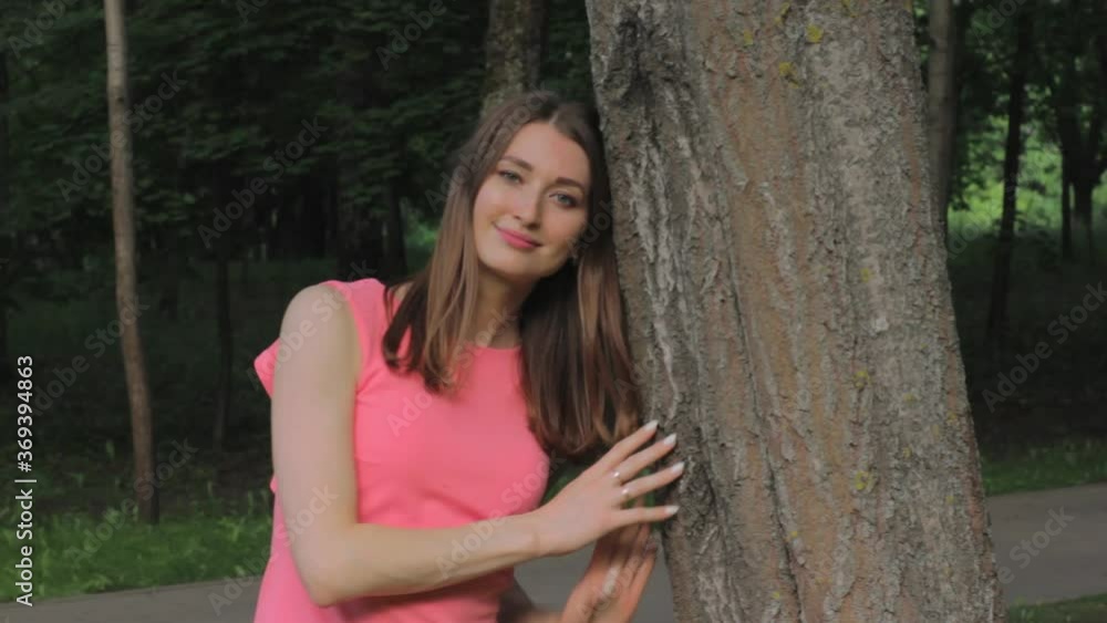 A young woman in a pink dress in a Park, clinging to a tree A young woman in a pink dress in a Park, clinging to a tree
