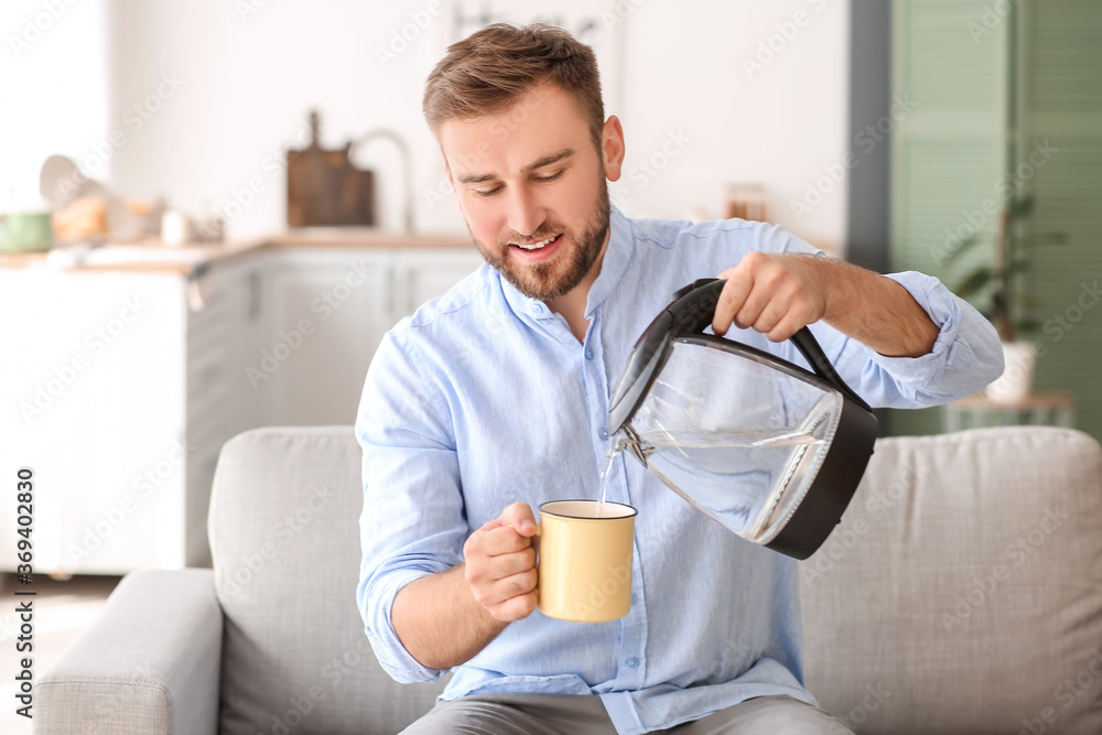 Man pouring hot boiled water from electric kettle into cup at home Man pouring hot boiled water from electric kettle into cup at home