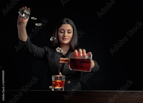 Attractive bartender girl pours an alcoholic drink into a glass and throws pieces of ice.