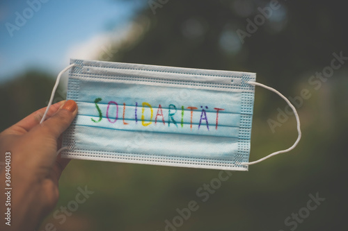 A medical face mask on which the word solidarity is written in colourful letters. Wearing face masks to protect against others during the Corona pandemic.