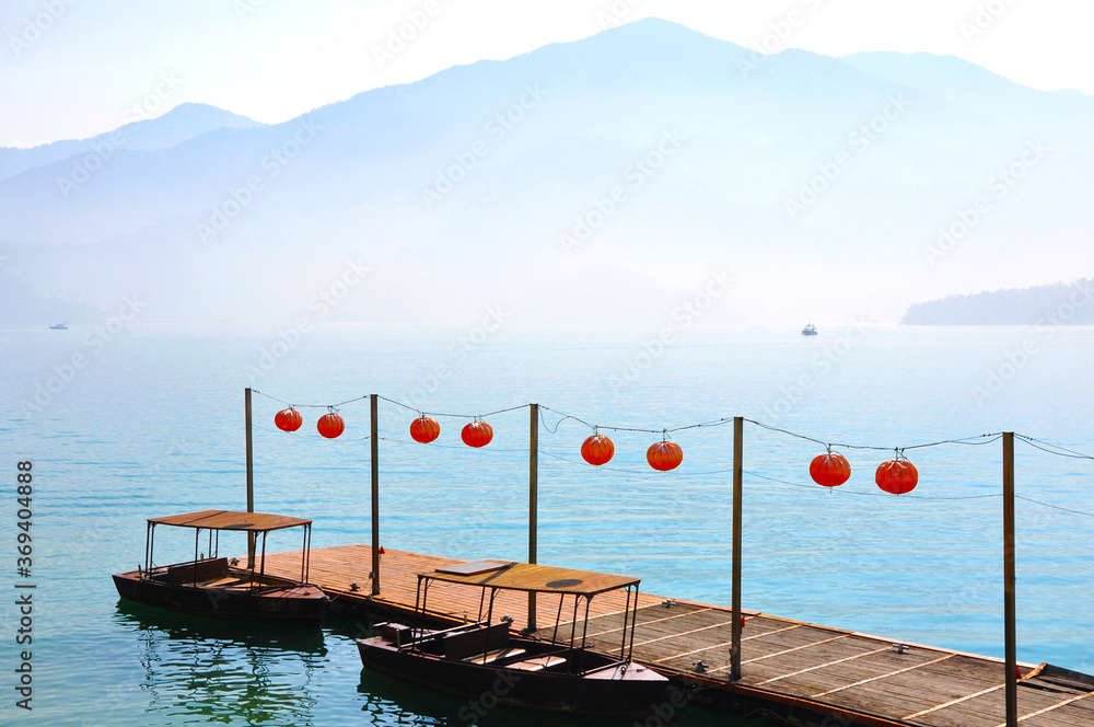 Obraz premium Wooden pier with old boats and red chinese lanterns on the beautiful misty morning at Sun Moon lake, Taiwan